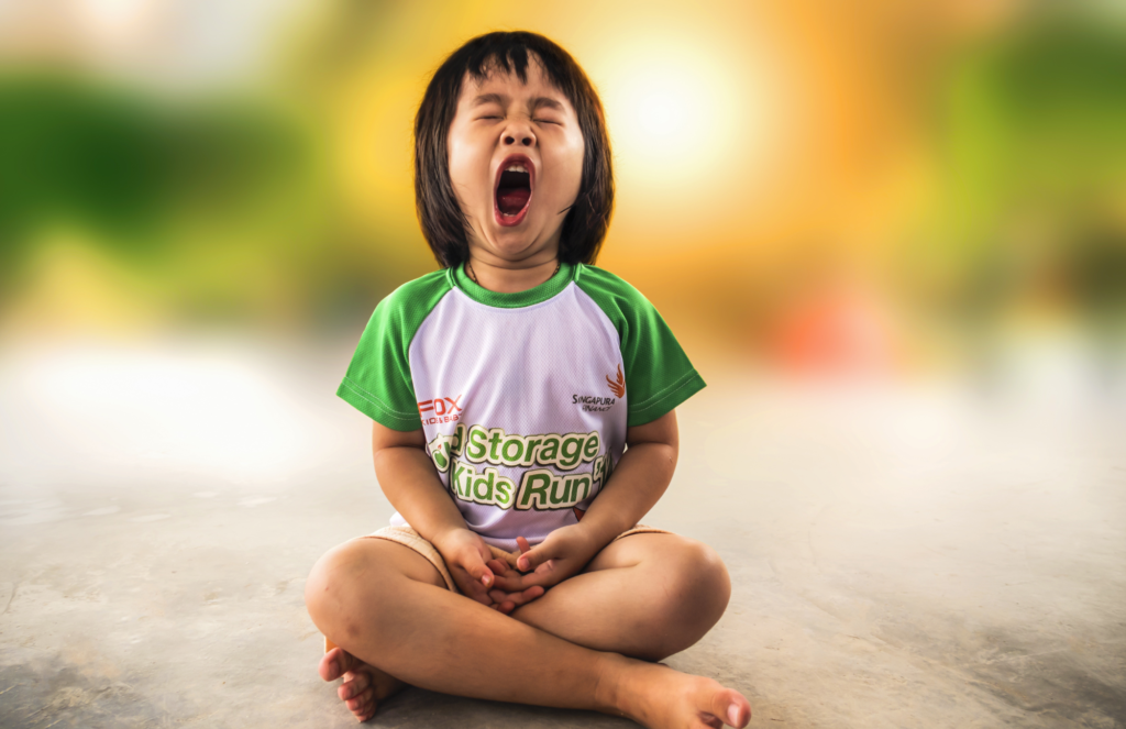 A little child sitting cross-legged. They are yawning widely.