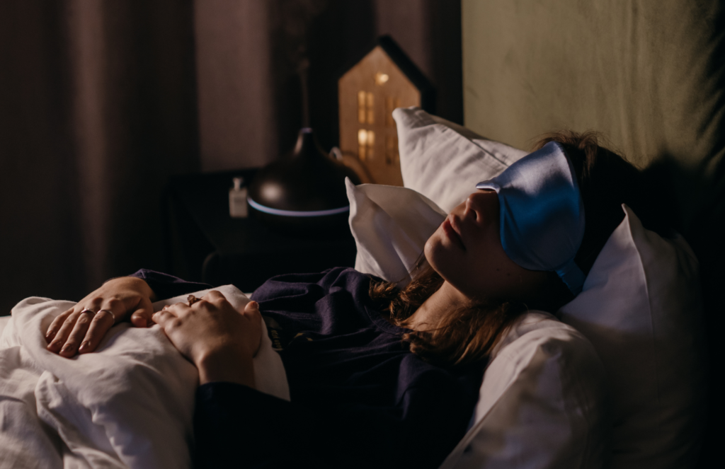 A woman resting in her bed on fluffy pillows with an eye mask on, getting good sleep