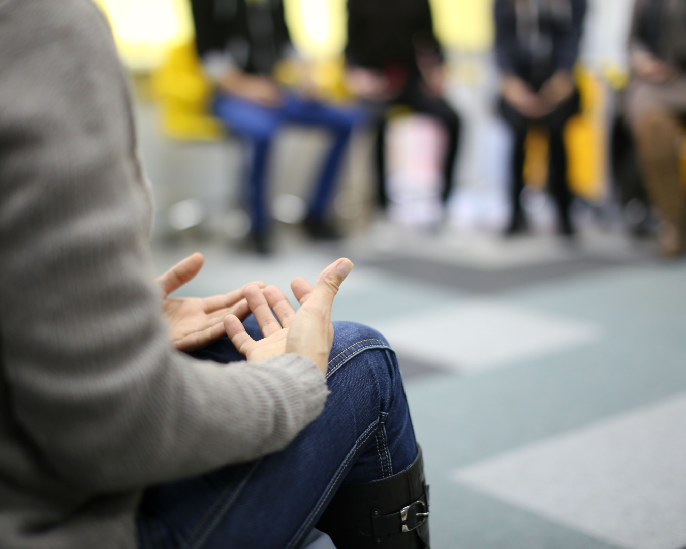 A close up of an individual talking with their hands, their face not visable. In the background you can see other group participants with whom the individual is sharing.