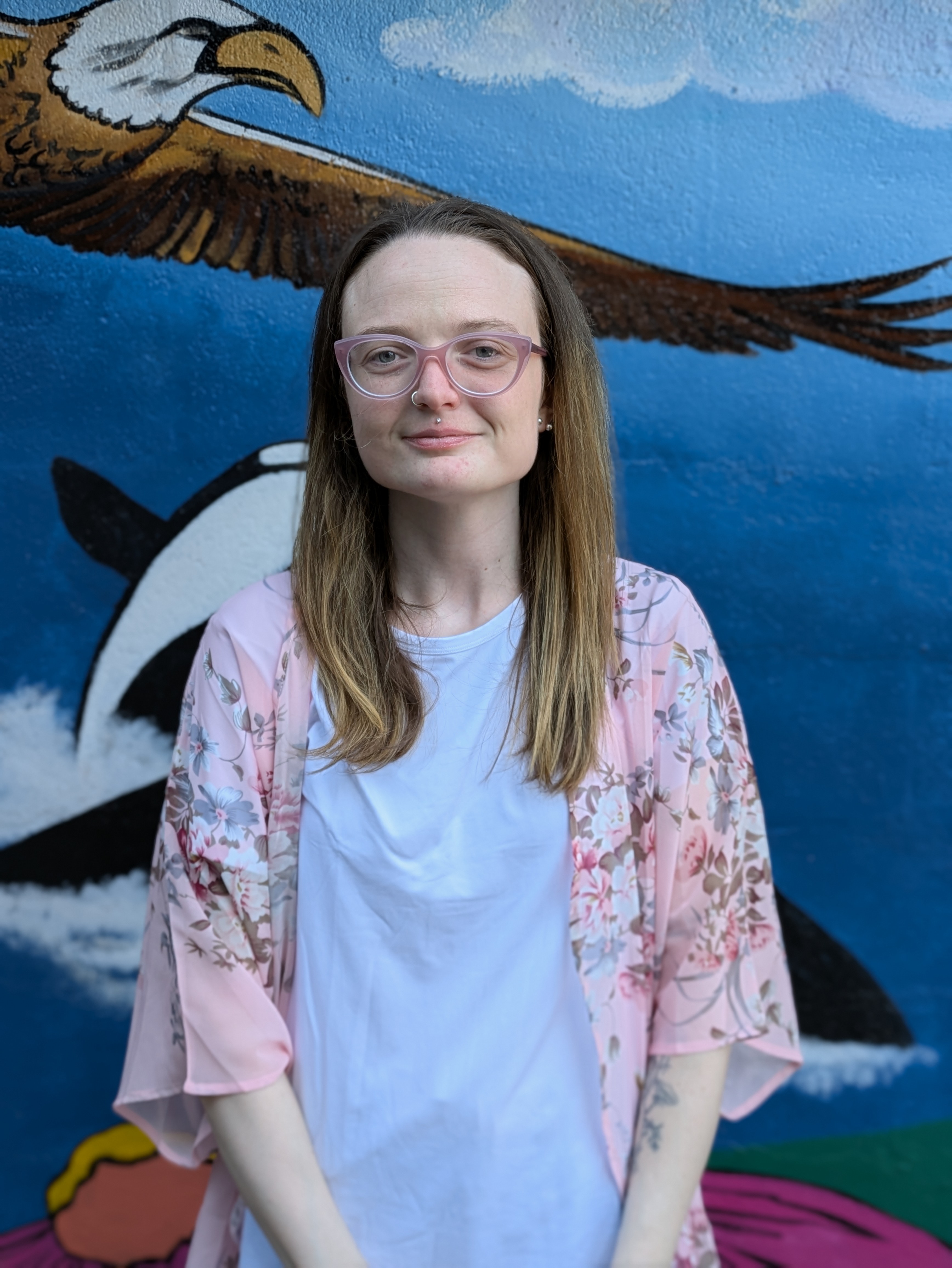 A picture of Abby Feinstein standing in front of the mural at Ancora Wellness